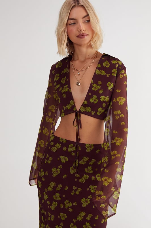 Chiffon fabric with a crinkle texture for added dimension
        Plunging V-neckline with tie-front detail
        Fluted sleeves for a dramatic flair
        Cropped length to showcase your midriff
        Ditsy floral print for a feminine touch
    
    Embrace the boho-chic aesthetic with this captivating Ditsy Crinkle Chiffon Tie Front Fluted Sleeve Crop Top from NastyGal. The lightweight chiffon fabric drapes beautifully, while the crinkle texture adds an intriguing visual element. The plunging V-neckline with a tie-front detail allows for adjustable coverage, making it perfect for various casual occasions. The fluted sleeves create a romantic silhouette, adding movement and grace to your ensemble. Pair this crop top with high-waisted jeans and ankle boots for a trendy daytime look, or style it with a flowing maxi skirt and sandals for a relaxed garden party. The versatile design makes it ideal for family gatherings, brunch dates, or casual outings with friends. Layer with delicate gold necklaces to complement the neckline and add a touch of glamour to this effortlessly stylish piece.