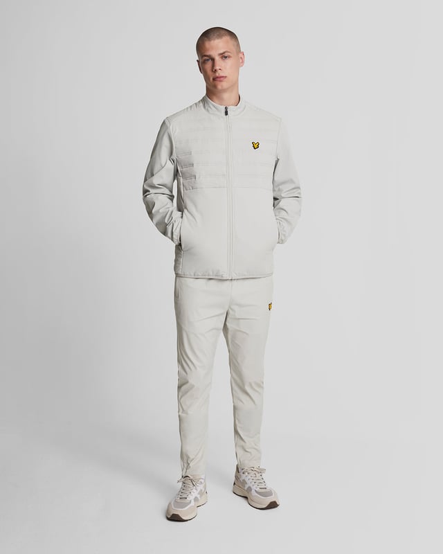 De Lyle & Scott sportcollectie is ontworpen om er goed uit te zien, of je nu in actie bent of aan de zijlijn staat. Deze Hybride Double Baffle Jacket heeft een gewatteerd voorpaneel en is gemaakt van een technische nylon- en elastaanmix voor extra rek en bewegingsvrijheid. De jas heeft een ritssluiting aan de voorkant en een elastische zoom en manchetten. \n- Kraag met hoge sluiting \n- Ritssluiting aan de voorkant \n- Gewatteerd paneel aan de voorkant \n- Lange mouwen \n- Zijzakken met rits \n- Elastische zoom en manchetten \n- Samenstelling: 90% nylon, 10% elastaan