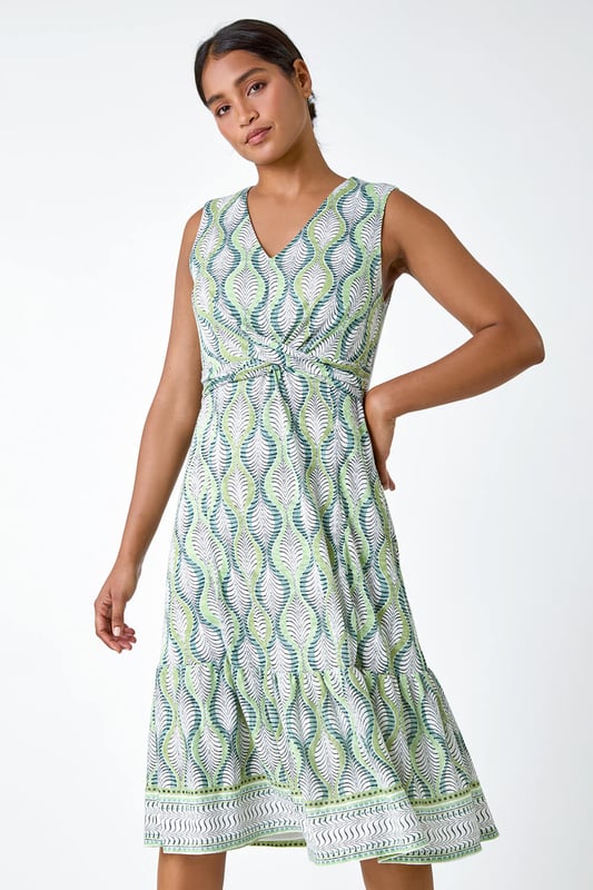 Twist Front Leaf Print Stretch Dress from Roman. Add a touch of nature to your Spring wardrobe with this stunning twist front dress. The abstract leaf print creates a fresh and playful feel, perfect for the season. The sleeveless design and v-neckline offer a feminine touch, while the knot detail at the waist flatters your figure. With its frill hem, stretch jersey fabric and burnout border print, it ensures all-day comfort and a flattering fit. Pair this midi dress with a casual denim jacket for an effortlessly chic day ensemble.