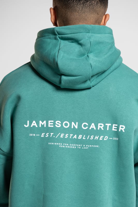 This 'Est' oversized hoodie from Jameson Carter is an everyday essential. Features dropped shoulder, hood, kangaroo pocket, ribbed elasticated cuffs and waistband and Jameson Carter chest and back branding details. This hoody is made from cotton blend fabric and the inside is lined with premium soft fleece to ensure comfort.