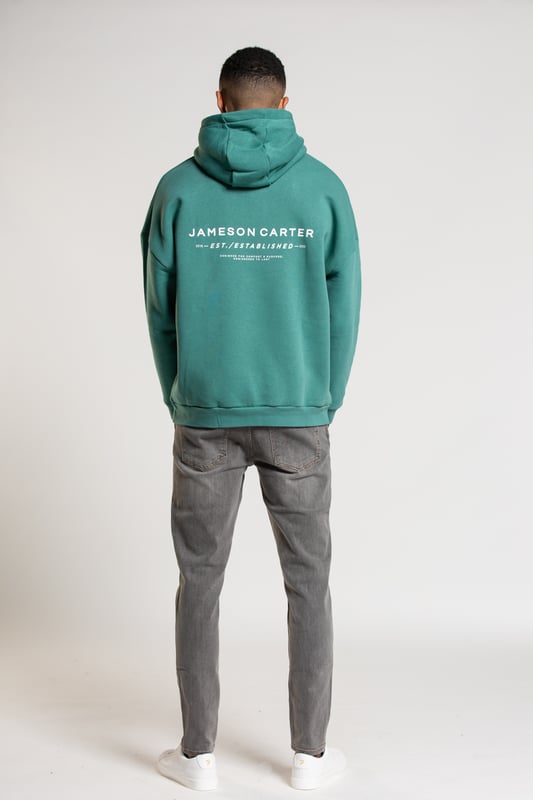 This 'Est' oversized hoodie from Jameson Carter is an everyday essential. Features dropped shoulder, hood, kangaroo pocket, ribbed elasticated cuffs and waistband and Jameson Carter chest and back branding details. This hoody is made from cotton blend fabric and the inside is lined with premium soft fleece to ensure comfort.