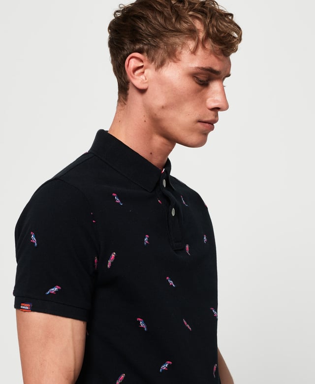 Superdry men's Bermuda polo shirt. This classic style polo shirt features short sleeves, two button fastening and an all over embroidered pattern. Finished with a Superdry logo tab on the hem and on one sleeve. Will look great with a pair of jeans or shorts and trainers this season.