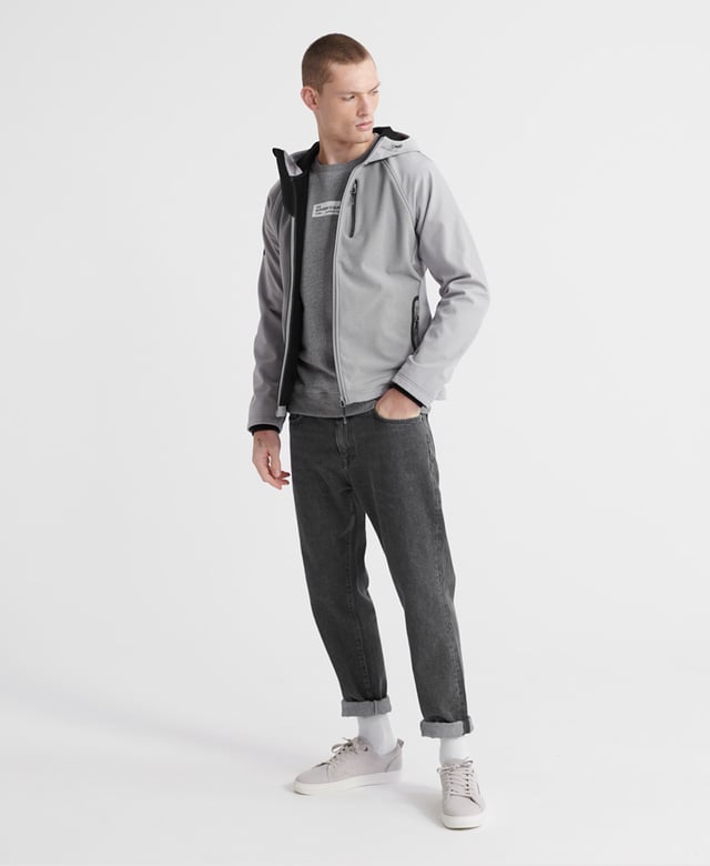 Superdry men's hooded Softshell jacket. Taking inspiration from hiking-wear, this softshell offers all the comfort of your favourite hoodie combined with the protection of a jacket. Featuring a practical hood with a bungee cord adjuster, full-length zip fastener, two front pockets with stormseal zip fastenings and reflective trims and a single zipped chest pocket with reflective trim. The hem has a bungee cord adjuster and the ribbed cuffs combine to keep you comfortable. Inside, the full fleece bonded lining forms two poacher style pockets for added practicality. The jacket is finished with Superdry branded zip pulls and a logo patch on the right sleeve.