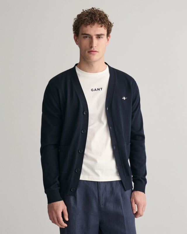 This durable and sophisticated cardigan from GANT is crafted in 100% cotton. Cut for a regular fit, it features a V-neck, knitted pockets, branded corozo buttons and ribbed detailing at the hem and cuffs. This piece is accented with a GANT shield graphic embroidered at the chest. 

Regular fit
V-neck
Knitted pockets
Rib detailing at hem and cuffs
GANT graphic embroidered at chest

100% cotton
8030556
 