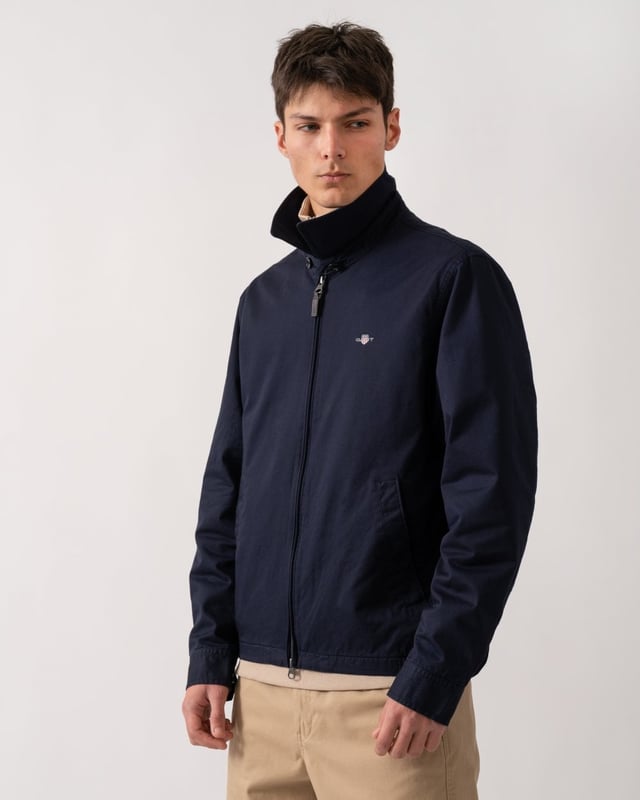 This jacket takes inspiration from GANT's beloved windcheater design, incorporating updated elements for the new season. Crafted from a water-repellent cotton twill shell, it is half-lined to shield against the cold while ensuring breathability. Designed for a regular fit that sits just above the hips, it features a partly elasticated hem for added comfort. Additional details include a front zip closure with a leather extender, slanted side welt pockets with hidden press buttons, two interior jetted pockets, and buttoned cuffs. It is finished with logo embroidery at the chest and a signature branded locker loop at the back. 

Regular fit
Above hip length
Water-repellent (DWR treatment)
Two outer and inner pockets

Shell - 100% Cotton, Upper Back Lining - 100% Cotton, Sleeve Lining - 100% Recycled Polyester 
7006494