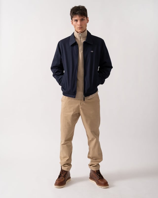 This jacket takes inspiration from GANT's beloved windcheater design, incorporating updated elements for the new season. Crafted from a water-repellent cotton twill shell, it is half-lined to shield against the cold while ensuring breathability. Designed for a regular fit that sits just above the hips, it features a partly elasticated hem for added comfort. Additional details include a front zip closure with a leather extender, slanted side welt pockets with hidden press buttons, two interior jetted pockets, and buttoned cuffs. It is finished with logo embroidery at the chest and a signature branded locker loop at the back. 

Regular fit
Above hip length
Water-repellent (DWR treatment)
Two outer and inner pockets

Shell - 100% Cotton, Upper Back Lining - 100% Cotton, Sleeve Lining - 100% Recycled Polyester 
7006494