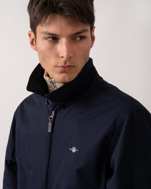 This jacket takes inspiration from GANT's beloved windcheater design, incorporating updated elements for the new season. Crafted from a water-repellent cotton twill shell, it is half-lined to shield against the cold while ensuring breathability. Designed for a regular fit that sits just above the hips, it features a partly elasticated hem for added comfort. Additional details include a front zip closure with a leather extender, slanted side welt pockets with hidden press buttons, two interior jetted pockets, and buttoned cuffs. It is finished with logo embroidery at the chest and a signature branded locker loop at the back. 

Regular fit
Above hip length
Water-repellent (DWR treatment)
Two outer and inner pockets

Shell - 100% Cotton, Upper Back Lining - 100% Cotton, Sleeve Lining - 100% Recycled Polyester 
7006494