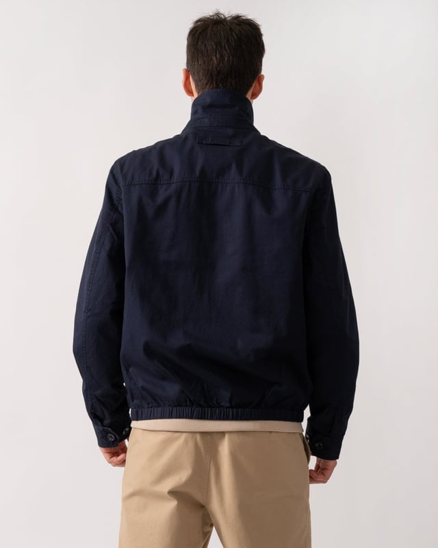 This jacket takes inspiration from GANT's beloved windcheater design, incorporating updated elements for the new season. Crafted from a water-repellent cotton twill shell, it is half-lined to shield against the cold while ensuring breathability. Designed for a regular fit that sits just above the hips, it features a partly elasticated hem for added comfort. Additional details include a front zip closure with a leather extender, slanted side welt pockets with hidden press buttons, two interior jetted pockets, and buttoned cuffs. It is finished with logo embroidery at the chest and a signature branded locker loop at the back. 

Regular fit
Above hip length
Water-repellent (DWR treatment)
Two outer and inner pockets

Shell - 100% Cotton, Upper Back Lining - 100% Cotton, Sleeve Lining - 100% Recycled Polyester 
7006494