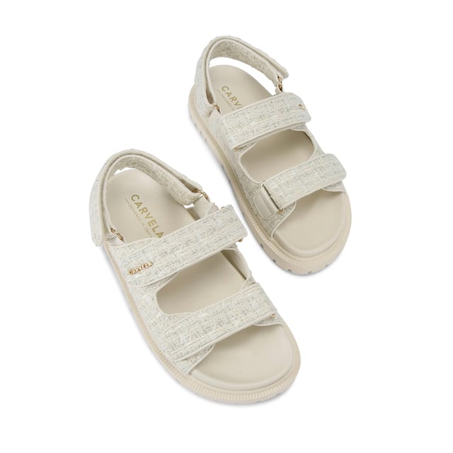 The Carvela Rosa Sandal is crafted in a cream tweed fabric. There is overstitch quilting in a diamond style across the upper straps. There is a gold branding detail on the top strap.