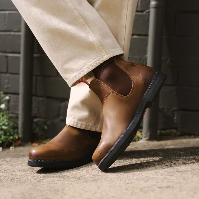 Presentamos las botas Rossi 607 Booma, una fusión perfecta de estilo, durabilidad y rendimiento inigualable. Estas botas Chelsea, confeccionadas con cuero de grano completo marrón de primera calidad con un llamativo refuerzo burdeos, están diseñadas para satisfacer las demandas de entornos de trabajo difíciles y aventuras urbanas, al mismo tiempo que ofrecen una comodidad excepcional y una estética destacada. Características principales: Construcción de cuero de grano completo de primera calidad: hechas de cuero de grano completo marrón de alta calidad, estas botas brindan una durabilidad excepcional y un aspecto pulido y atemporal que supera a competidores como Blundstone. Llamativos refuerzos y lengüetas de tiro burdeos: los refuerzos elásticos burdeos vibrantes combinados con resistentes lengüetas de tiro no solo elevan el estilo, sino que también hacen que ponerse estas botas sea muy fácil. Suela Mud-Shed Tread: diseñada para exteriores, la innovadora suela Mud-Shed brinda un agarre y una comodidad excepcionales al tiempo que evita la acumulación de escombros, ideal para la agricultura, la jardinería, el paisajismo o cualquier terreno. Suela antideslizante certificada: diseñada para brindar estabilidad en superficies resbaladizas o irregulares, lo que garantiza la máxima seguridad en cualquier entorno, desde senderos fangosos hasta pisos pulidos. Resistencia al aceite y al ácido: con una suela que resiste al aceite y al ácido, estas botas son perfectamente adecuadas para trabajos exigentes en granjas, fábricas, cocinas y otros lugares de trabajo desafiantes. Interior forrado en cuero: el forro de cuero transpirable ofrece una comodidad superior, manteniendo sus pies frescos y sujetos durante largas horas de uso. La bota Chelsea Rossi Boots 607 Booma es más que un simple calzado: es una compañera versátil diseñada para los desafíos más difíciles de la vida y los momentos más elegantes. Desde los caminos de tierra del campo hasta las bulliciosas calles de la ciudad, estas botas brindan la combinación perfecta de funcionalidad resistente y sofisticación moderna. Con sus distintivos acentos burdeos, artesanía duradera y comodidad durante todo el día, la 607 Booma es la mejor opción para aquellos que exigen estilo y rendimiento en cada paso.