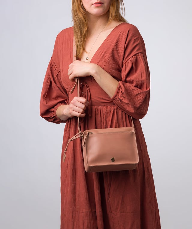 The 'Aurora' cross body bag from Conkca London elevates this classic design with a natural leather exterior for a beautifully smooth finish. A zip-over top conceals the central 100% cotton lined compartment alongside a handy slip pocket. Additional storage space is provided by a zipped pocket and slip pocket, ideal for on-the-go storage. The accessory comes with an adjutable leather strap secured with rustic gold metal fittings; this is all finished with the iconic Conkca London logo and charm.