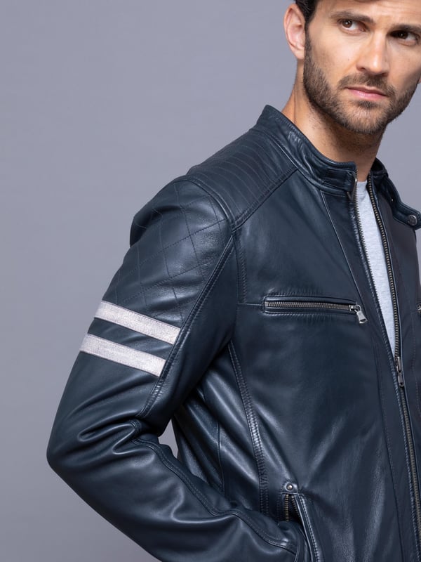 With all the hallmarks of a Lakeland favourite jacket, Charlie is a contemporary update to a traditional cafe racer design.
A slim fit biker inspired jacket with a cafe racer classic silhouette, buckle press stud collar, press stud cuffs and side fastening and contrasting stripe. For fans of the motorcycle era this jacket gives a nod to the racing heritage. The striking navy design with quilted shoulder stitching and coloured leather stripes on the sleeve is crafted from UK sourced aniline leather for a soft sheen. The Charlie biker is a garment that will age beautifully the more you wear it, creating a fit unique to the wearer.