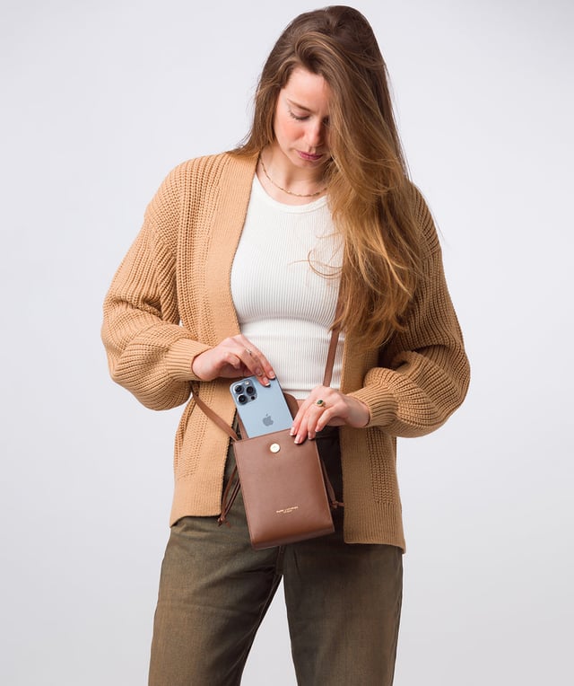 The 'Kiana' cross body phone bag from the Pure Luxuries Marylebone Collection is handcrafted from high-quality, genuine Nappa leather with a natural super-soft touch. The minimalistic fold-over top is secured by a gold-coloured magnetic press stud. This practical design is the perfect place to keep your phone safe and features a tassel design on the exterior. Lined with 100% cotton for a flawless finish and comes with a matching and adjustable slim leather strap with a maximum drop length of 65cm. The minimalist Pure Luxuries logo is embossed in gold foil for a beautifully simple finishing touch.
