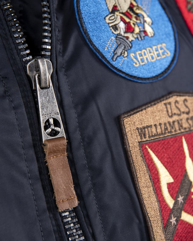 Der einzigartige Top Gun Stil spiegelt sich in dieser hippen Nylonjacke. Sie ist gut gefüttert und besitzt die typische Ärmeltasche mit Reißverschluss - so lässt sich das Tragen dieser Jacke an Lässigkeit kaum überbieten. Der elastische Strick am Ärmelabschluss, Bund und am Kragen sorgt für eine ideale Passform. Optisch ansprechende Stickereien und ein weiches Innenfutter mit Bild schmücken diese Jacke. Zwei seitliche Taschen zum Einschieben mit Knopfverschluss bieten viel Stauraum. Hierfür sind im Inneren zwei zusätzliche Taschen verarbeitet. Diese Jacke ist der absoluter Hingucker für die kalte Jahreszeit.