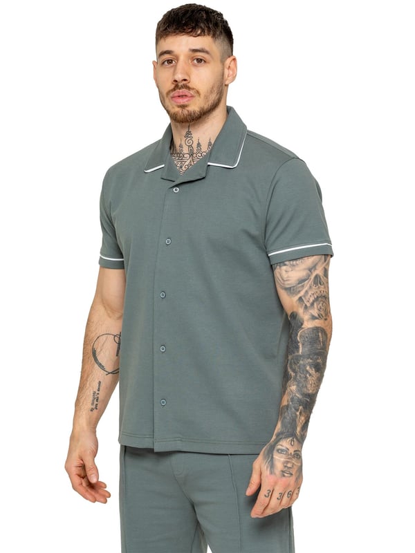 The Enzo Men's Piping Shirt is a stylish and versatile piece designed for both comfort and sophistication. Featuring a revere collar and white piping detail along the collar and sleeves, this button-up shirt offers a refined yet relaxed look. Crafted from premium fabric with stretch, it ensures ease of movement while maintaining a sleek silhouette. With a regular fit, short sleeves, and a stitched hem finish, this shirt is perfect for casual outings or smart-casual styling.