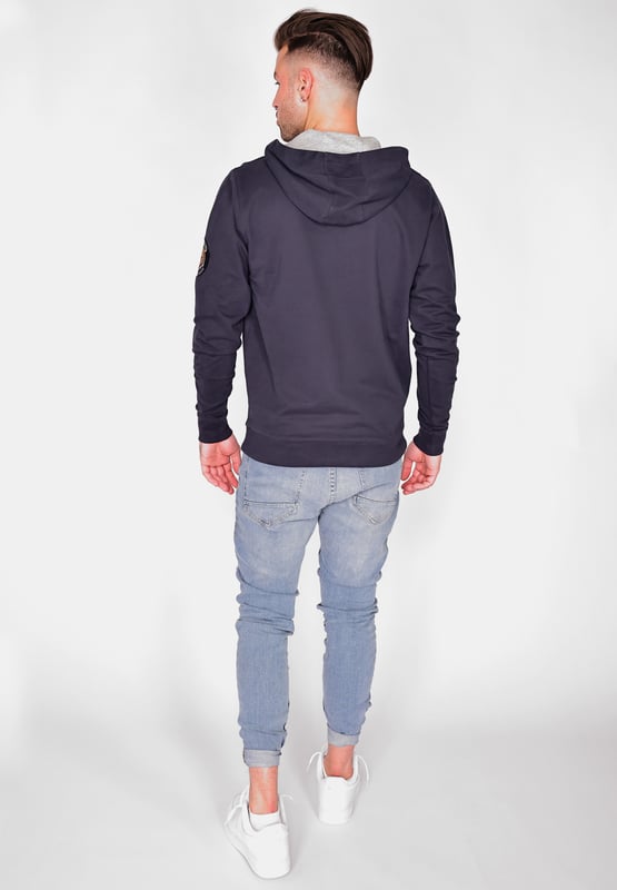 De unieke Top Gun stijl komt terug in deze moderne hoodie. Hij is voorzien van de typische patches op de bovenarm en unieke studs op de borst. Het elastische breisel bij de manchetten en tailleband zorgt voor een ideale pasvorm. De zachte stof en grote zak aan de voorkant bieden extra comfort. De hoodie heeft een capuchon met trekkoord en een stijlvolle print op de voorkant.