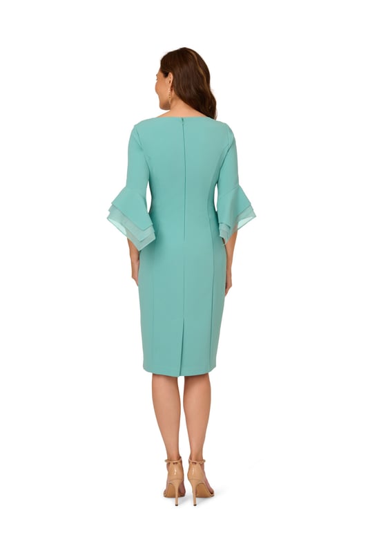 Dressed up meets versatile in this timeless sheath dress. This midi dress features a boat neckline, fitted silhouette through the body, and tiered three-quarter bell sleeves with organza accents. Crafted using knit crepe, this day dress has some stretch and no waist seam for a comfortable fit. A zipper back closure and a single pleat at the center back of the skirt hem completes the design.