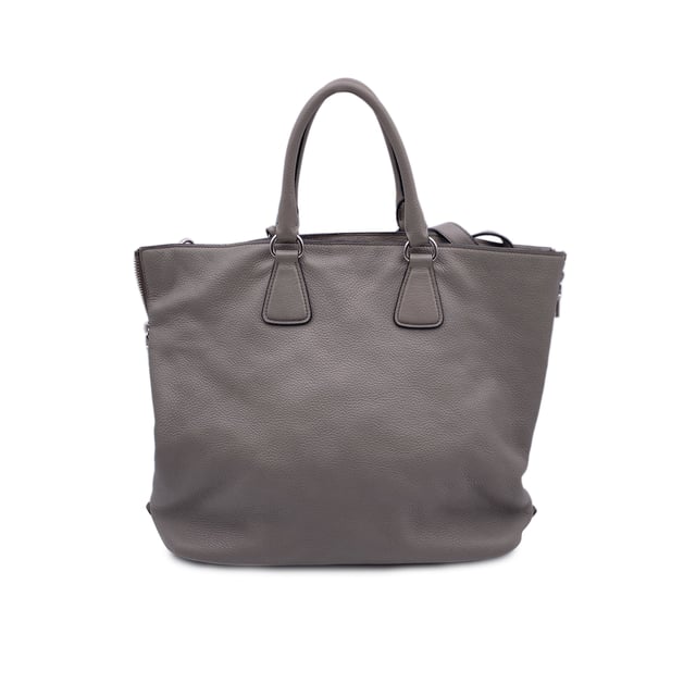 VINTAGE, UVP WIE NEU  
Schöne PRADA Tote-Bag aus strukturiertem Leder in Grau Taupe. Sie verfügt über doppelte, runde Obergriffe und einen verstellbaren sowie abnehmbaren Schultergurt. Auf der Vorderseite befindet sich die PRADA-Beschriftung in Silbermetall. Oberer Reißverschlussverschluss. 4 Fuß aus Metall am Boden. Die Tasche hat ein Hauptfach. Das Innere ist vollständig mit dem charakteristischen PRADA-Stoff ausgekleidet. 1 interne Reißverschlusstasche und 1 offene Tasche innen. Vier Metallfüße am Boden für Stil und Schutz. 'PRADA Milano'-Tag innen, kleines Etikett mit Zahlen in der Innenstasche. Zustand Bewertung: B - SEHR GUTER ZUSTAND  
Zustandsdetails: Einige kleine Kratzer (mit kleinen weißen Stellen) auf dem Leder aufgrund normaler Nutzung. Ein paar schwarze Flecken auf dem Leder durch normale Nutzung. Einige Gebrauchsspuren an den unteren Ecken. Einige leichte Kratzer auf der Oberfläche des Beschlags. Bitte überprüfen Sie die Fotos sorgfältig und fragen Sie, wenn Sie weitere Details benötigen oder zweifeln haben.  
Maße (cm):  
Tiefe: 15,2  
Höhe: 34,3  
Länge: 36,8  
Weitere Details: Staubbeutel? Ja  
Schlüssel? Nein  
Box? Nein  
Maße: Breite: 152 mm, Länge: 368 mm, Höhe: 343 mm