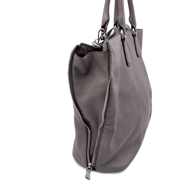 VINTAGE, UVP WIE NEU  
Schöne PRADA Tote-Bag aus strukturiertem Leder in Grau Taupe. Sie verfügt über doppelte, runde Obergriffe und einen verstellbaren sowie abnehmbaren Schultergurt. Auf der Vorderseite befindet sich die PRADA-Beschriftung in Silbermetall. Oberer Reißverschlussverschluss. 4 Fuß aus Metall am Boden. Die Tasche hat ein Hauptfach. Das Innere ist vollständig mit dem charakteristischen PRADA-Stoff ausgekleidet. 1 interne Reißverschlusstasche und 1 offene Tasche innen. Vier Metallfüße am Boden für Stil und Schutz. 'PRADA Milano'-Tag innen, kleines Etikett mit Zahlen in der Innenstasche. Zustand Bewertung: B - SEHR GUTER ZUSTAND  
Zustandsdetails: Einige kleine Kratzer (mit kleinen weißen Stellen) auf dem Leder aufgrund normaler Nutzung. Ein paar schwarze Flecken auf dem Leder durch normale Nutzung. Einige Gebrauchsspuren an den unteren Ecken. Einige leichte Kratzer auf der Oberfläche des Beschlags. Bitte überprüfen Sie die Fotos sorgfältig und fragen Sie, wenn Sie weitere Details benötigen oder zweifeln haben.  
Maße (cm):  
Tiefe: 15,2  
Höhe: 34,3  
Länge: 36,8  
Weitere Details: Staubbeutel? Ja  
Schlüssel? Nein  
Box? Nein  
Maße: Breite: 152 mm, Länge: 368 mm, Höhe: 343 mm
