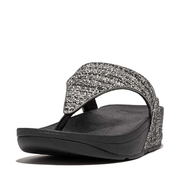 Women's Fit Flop Lulu Shimmerweave Toe-Post Sandals in Black FitFlop's bestselling Lulu sandals boast a timeless triangular vamp softly padded uppers and a soft microfibre toe post. Featuring FitFlop's Microwobbleboard™ midsoles for unbeatable comfort. This season in a sparkling finely ribbed glitz mesh (with metallic pearlised faux-leather side panels for extra lustre). Beautiful. Versatile. The sophisticated shimmer means these work with multiple looks - dress yours up or down wear day through to night.Ergonomically engineered to help optimize your body's alignment natural movement & energyLight pressure-diffusing Microwobbleboard midsole - triple-density cushioning follows 3 footstep stages (firm heel-soft middle-medium at toes)Natural arch supportAverage to wide fitGrip level 1 - everyday use-road treadThese shoes have been granted the APMA* Seal of Acceptance for footwear found to promote good foot health*American Podiatric Medical Association