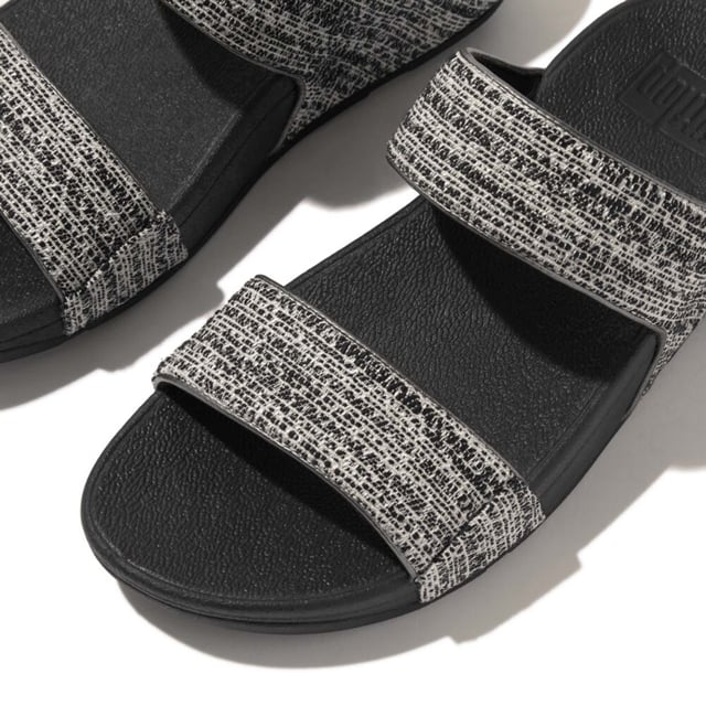 Women's Fit Flop Lulu Shimmerweave Sliders in Black De Lulu slippers van FitFlop zijn klassiekers. Blijvend populair, ze zijn zacht gevoerd en kunnen omhoog of omlaag gekleed worden. Ze staan op FitFlop's legendarische super dempende Microwobbleboard™ tussenzool. Dit seizoen uitgevoerd in een glinsterende structuurstof met een chique 'tweedy' uitstraling. Afgerand met metallic parelmoeren biezen van imitatieleer voor extra glans. Subtiel glinsterende sandalen die je overal bij kunt dragen en prachtig zijn van dag tot nacht.