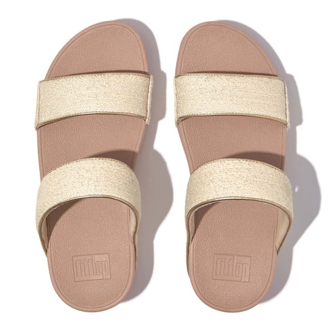 Women's Fit Flop Lulu Shimmerweave Sliders in Stone De Lulu slippers van FitFlop zijn klassiekers. Blijvend populair, ze zijn zacht gevoerd en kunnen omhoog of omlaag gekleed worden. Ze staan op FitFlop's legendarische super dempende Microwobbleboard™ tussenzool. Dit seizoen uitgevoerd in een glinsterende stof met een chique 'tweedy' uitstraling. Afgerand met metallic parelmoeren biezen van imitatieleer voor extra glans. Subtiel glinsterende sandalen die je overal bij kunt dragen en prachtig zijn van dag tot nacht.