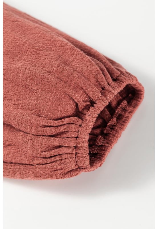 Blusa de color sólido en rojo mineral  
Tejido texturizado para mayor profundidad  
Detalle de volantes en los bordes  
Escote en V para un aspecto elegante  
Mangas abullonadas para una silueta dramática  
Diseño versátil y atemporal  
Material: 85% Poliéster 10% Algodón 5% Elastano
