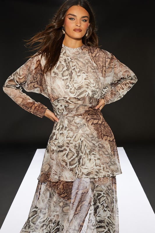 Chiffon fabric for a lightweight, flowing silhouette
        Pleated bodice adds texture and visual interest
        Sheer skirt creates an alluring, layered effect
        Maxi length for a dramatic, sweeping look
        Snake print pattern for a bold, edgy aesthetic
    
    Make a statement in this striking maxi dress from RUNWAY 1.8.1.8. The pleated bodice adds a touch of sophistication, while the sheer skirt creates an enchanting, layered effect that's perfect for daytime events. Style this versatile piece with ankle boots and a leather jacket for an edgy lunch date look, or pair it with flat sandals and oversized sunglasses for a chic garden party ensemble. The round neckline and long sleeves offer a modest touch, balancing the allure of the sheer skirt. This dress is ideal for those confident women who want to project a feminine yet daring style at casual gatherings or family events. The snake print pattern adds a bold twist to your wardrobe, ensuring you'll stand out in any crowd.