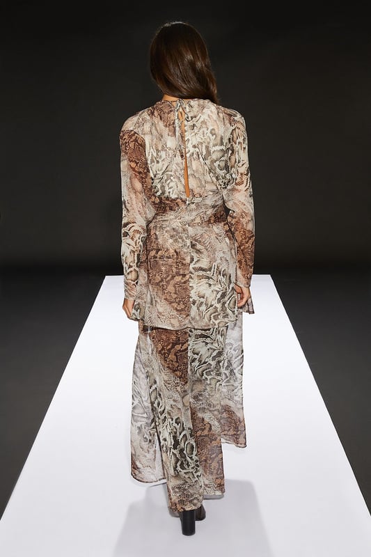 Chiffon fabric for a lightweight, flowing silhouette
        Pleated bodice adds texture and visual interest
        Sheer skirt creates an alluring, layered effect
        Maxi length for a dramatic, sweeping look
        Snake print pattern for a bold, edgy aesthetic
    
    Make a statement in this striking maxi dress from RUNWAY 1.8.1.8. The pleated bodice adds a touch of sophistication, while the sheer skirt creates an enchanting, layered effect that's perfect for daytime events. Style this versatile piece with ankle boots and a leather jacket for an edgy lunch date look, or pair it with flat sandals and oversized sunglasses for a chic garden party ensemble. The round neckline and long sleeves offer a modest touch, balancing the allure of the sheer skirt. This dress is ideal for those confident women who want to project a feminine yet daring style at casual gatherings or family events. The snake print pattern adds a bold twist to your wardrobe, ensuring you'll stand out in any crowd.