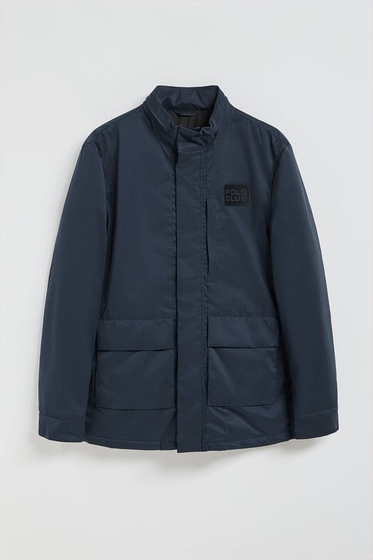 Der leichte Herrenparka Chelsea ist auf Funktionalität und Stil ausgelegt und kombiniert modernes Design mit klassischen Details. Die verdeckte Kapuze am Kragen sorgt für Vielseitigkeit und bietet bei Bedarf Schutz. Er verfügt über zwei aufgesetzte Taschen und eine verdeckte Brusttasche mit Reißverschluss. Der Hauptreißverschluss wird von einer Knopfleiste aus dem Hauptgewebe abgedeckt, die mit Druckknöpfen geschlossen wird und zusätzlichen Schutz vor Wind bietet. An der Innenseite befinden sich zwei Stopper an der Taille, mit denen Sie das Kleidungsstück nach Ihren Wünschen anpassen können. Details wie Zipper, Gummizüge und Stopper mit Logo sowie ein gummierter Aufnäher aus Twill mit dem Polo Club Logo auf der Brust verleihen dem Kleidungsstück eine exklusive und persönliche Note. Ideal für den modernen Mann, der ein leichtes, funktionelles Kleidungsstück mit einem Hauch von Raffinesse sucht.