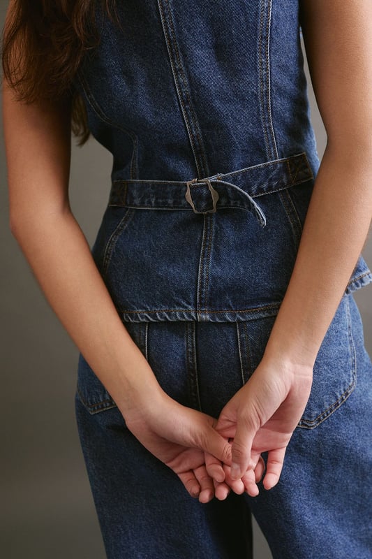 Sleek longline silhouette for a contemporary twist on classic denim
        Plunging V-neckline adds a touch of allure
        Button-front closure for easy wear and versatile styling
        Fitted waist with adjustable belt detail for a customised fit
        Crafted from sturdy denim fabric for long-lasting wear
    
    The Longline Denim Waistcoat from NastyGal is a versatile piece that seamlessly blends casual cool with a hint of sophistication. This sleeveless wonder can be styled in myriad ways to suit various occasions. For a laid-back daytime look, pair it with wide-leg jeans and trainers, as seen on our model. Layer it over a crisp white shirt and tailored trousers for a smart-casual ensemble perfect for family gatherings or informal work events. The adjustable belt allows you to cinch in the waist for a more defined silhouette, while the longline cut provides flattering coverage. Whether worn open as a vest or buttoned up as a standalone top, this denim waistcoat is sure to become a staple in your wardrobe, offering endless styling possibilities for the fashion-forward individual.