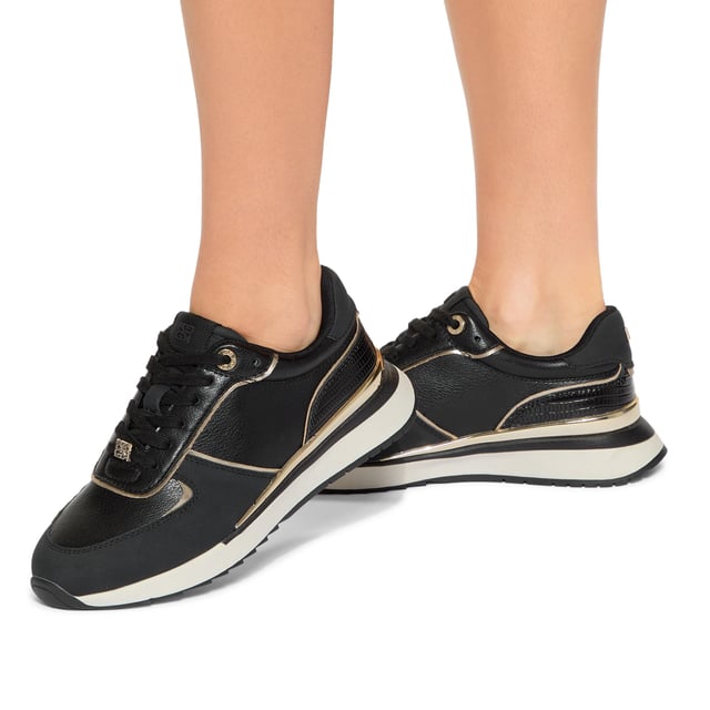The List is a white sneaker with black and metallic gold panels across the upper. The front laces up with gold tone hardware details.