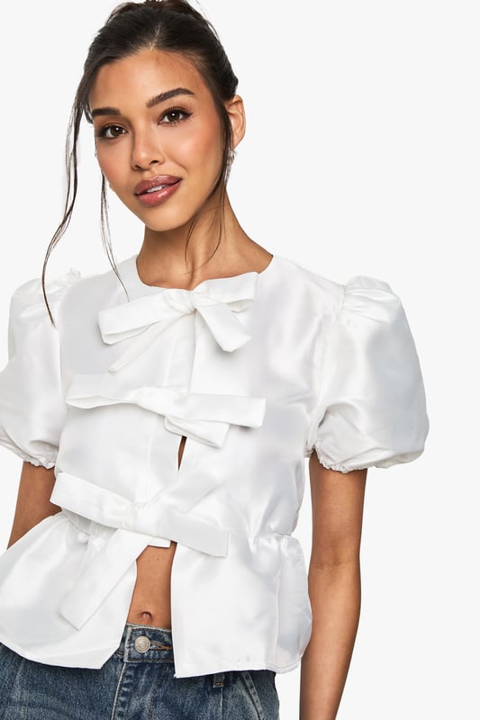 Charming taffeta blouse with eye-catching lace-up detail
        Elegant puff sleeves for a romantic silhouette
        Ruffled front adds a touch of whimsy and femininity
        Peplum waist creates a flattering shape
        Versatile design suitable for both casual and dressy occasions
    
    This enchanting taffeta blouse is the perfect addition to your festive wardrobe. The lace-up detail at the neckline adds a playful touch, while the puff sleeves and ruffled front create a romantic, feminine silhouette. The peplum waist cinches in to flatter your figure, making it an ideal choice for Christmas parties or celebratory dinners. Style it with sleek black trousers and statement earrings for a chic evening look, or pair it with your favourite jeans and ankle boots for a more relaxed daytime ensemble. The versatility of this top allows you to dress it up or down, ensuring you'll shine at any holiday gathering. Whether you're sipping mulled wine at a festive market or dancing the night away at a Christmas bash, this blouse will keep you looking stylish and feeling confident throughout the season.