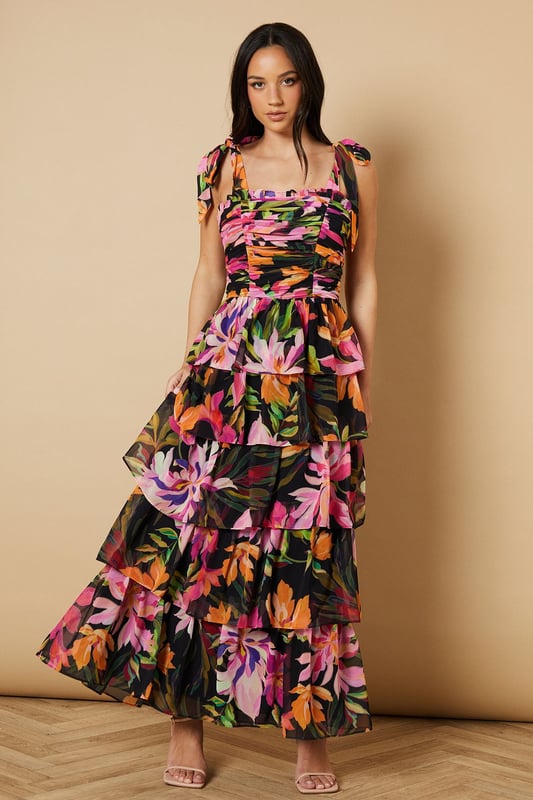 Feminine ruched bodice with elegant gathering that creates a flattering silhouette
        Charming tie straps with ruffle detail for an adjustable fit and pretty finish
        Tiered midi skirt design with beautiful movement and volume
        Striking floral print that captures Oasis's signature feminine aesthetic
        Square neckline that frames the dcolletage beautifully
    
    This enchanting midi dress from Oasis embodies romantic charm with its thoughtfully designed ruched bodice and playful tiered skirt. The delicate tie straps can be adjusted to your perfect fit, while the ruffle detailing adds a touch of whimsy to this occasion-ready piece. Style with strappy heeled sandals as seen on our model for garden parties and summer weddings, or dress it up with statement earrings and an elegant clutch for formal events. The flowing tiered design creates beautiful movement as you walk, making it ideal for those special moments that call for something truly memorable. For cooler evenings, layer with a lightweight pashmina or tailored blazer to maintain that refined silhouette whilst staying comfortable throughout your event.