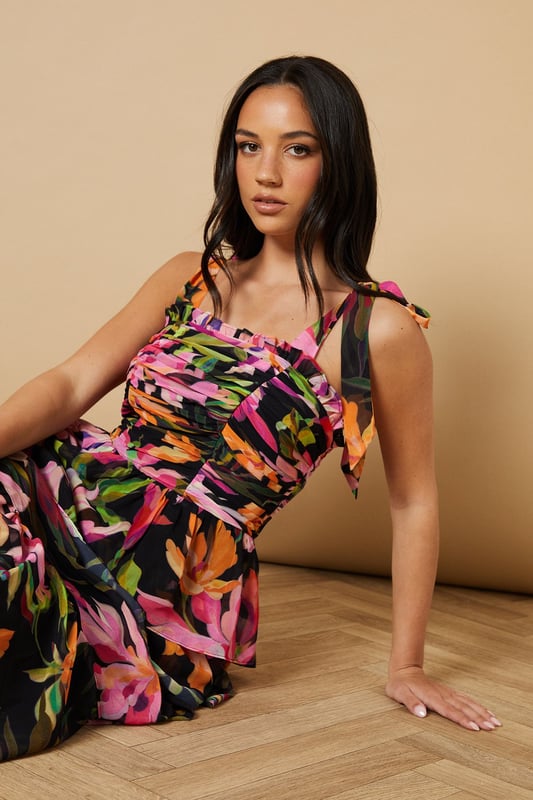 Feminine ruched bodice with elegant gathering that creates a flattering silhouette
        Charming tie straps with ruffle detail for an adjustable fit and pretty finish
        Tiered midi skirt design with beautiful movement and volume
        Striking floral print that captures Oasis's signature feminine aesthetic
        Square neckline that frames the dcolletage beautifully
    
    This enchanting midi dress from Oasis embodies romantic charm with its thoughtfully designed ruched bodice and playful tiered skirt. The delicate tie straps can be adjusted to your perfect fit, while the ruffle detailing adds a touch of whimsy to this occasion-ready piece. Style with strappy heeled sandals as seen on our model for garden parties and summer weddings, or dress it up with statement earrings and an elegant clutch for formal events. The flowing tiered design creates beautiful movement as you walk, making it ideal for those special moments that call for something truly memorable. For cooler evenings, layer with a lightweight pashmina or tailored blazer to maintain that refined silhouette whilst staying comfortable throughout your event.
