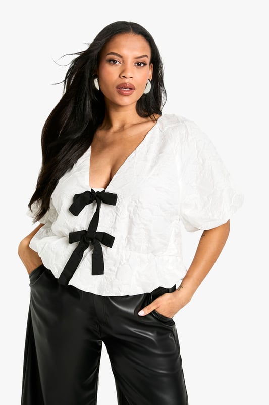 Striking jacquard texture for visual interest
        Plunging V-neckline with contrasting bow details
        Voluminous puff sleeves for dramatic flair
        Fitted waist creates a flattering silhouette
        Versatile design suitable for various body types
    
    Make a bold statement with this eye-catching jacquard kittel top. The contrasting bow details at the neckline add a touch of playful sophistication, while the voluminous puff sleeves create a dramatic silhouette that's sure to turn heads. Perfect for a night out on the town, this top pairs beautifully with wide-leg trousers and statement earrings, as shown on our model. The fitted waist accentuates your curves, making it a flattering choice for all body types. Whether you're heading to a trendy bar or meeting friends for cocktails, this versatile piece will help you radiate confidence and style. Dress it up with sleek heels and a clutch for a more polished look, or keep it casual with trainers and a leather jacket for an edgy urban vibe.