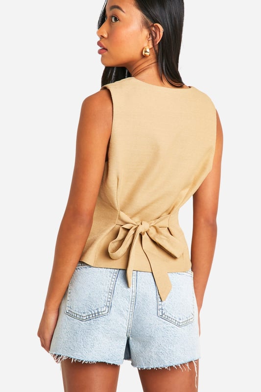 Textured woven crepe fabric for added visual interest
        Sleeveless design with a collared neckline
        Button-front closure for easy wear
        Relaxed fit for comfortable, effortless style
        Charming bow-tie detail at the back for a feminine touch
    
    This structured woven vest from Boohoo is a versatile piece that can effortlessly transition from day to night. The relaxed fit and textured crepe fabric create a laid-back yet polished look, perfect for various casual occasions. Style it with denim shorts and trainers for a chic daytime ensemble, or pair it with tailored trousers and heels for a more sophisticated evening outfit. The button-front closure allows for customisable styling, while the unexpected bow-tie detail at the back adds a playful twist. Ideal for family gatherings, brunches with friends, or casual Fridays at the office, this vest is a must-have addition to your wardrobe. Its adaptable nature makes it suitable for layering in cooler weather or wearing on its own during warmer months, ensuring year-round wearability.