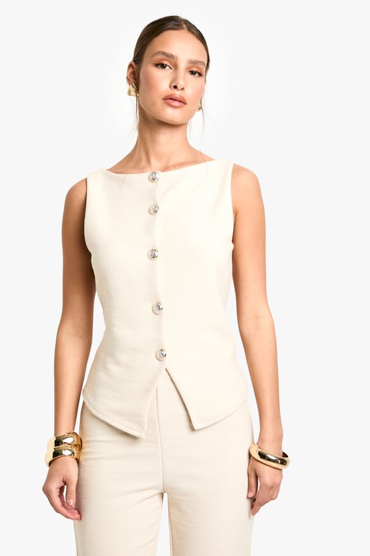 Textured knitted waistcoat with elegant boat neckline for a sophisticated silhouette
        Sleeveless design with clean-cut edges perfect for layering or wearing alone
        Decorative button-through front with distinctive statement buttons
        Structured fit that gently contours the body for a flattering shape
        Versatile length that pairs beautifully with coordinating trousers or contrasting bottoms
    
    This textured waistcoat reimagines casual dressing with its contemporary structured design. The sleek boat neckline and decorative button detailing create a refined aesthetic that transitions effortlessly from day to evening. Style with the matching trousers as seen on our model for a coordinated ensemble that works brilliantly for family gatherings or casual brunches. For a more relaxed approach, pair with wide-leg jeans and trainers, adding layered gold jewellery for a touch of everyday glamour. The versatile nature of this piece allows for customisation to suit your personal style - try layering over a fitted long-sleeve top when temperatures drop or wearing alone with statement accessories for warmer days. Perfect for those seeking a polished yet comfortable look for casual occasions.