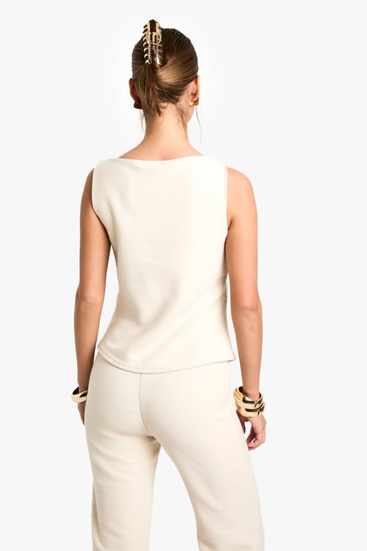 Textured knitted waistcoat with elegant boat neckline for a sophisticated silhouette
        Sleeveless design with clean-cut edges perfect for layering or wearing alone
        Decorative button-through front with distinctive statement buttons
        Structured fit that gently contours the body for a flattering shape
        Versatile length that pairs beautifully with coordinating trousers or contrasting bottoms
    
    This textured waistcoat reimagines casual dressing with its contemporary structured design. The sleek boat neckline and decorative button detailing create a refined aesthetic that transitions effortlessly from day to evening. Style with the matching trousers as seen on our model for a coordinated ensemble that works brilliantly for family gatherings or casual brunches. For a more relaxed approach, pair with wide-leg jeans and trainers, adding layered gold jewellery for a touch of everyday glamour. The versatile nature of this piece allows for customisation to suit your personal style - try layering over a fitted long-sleeve top when temperatures drop or wearing alone with statement accessories for warmer days. Perfect for those seeking a polished yet comfortable look for casual occasions.