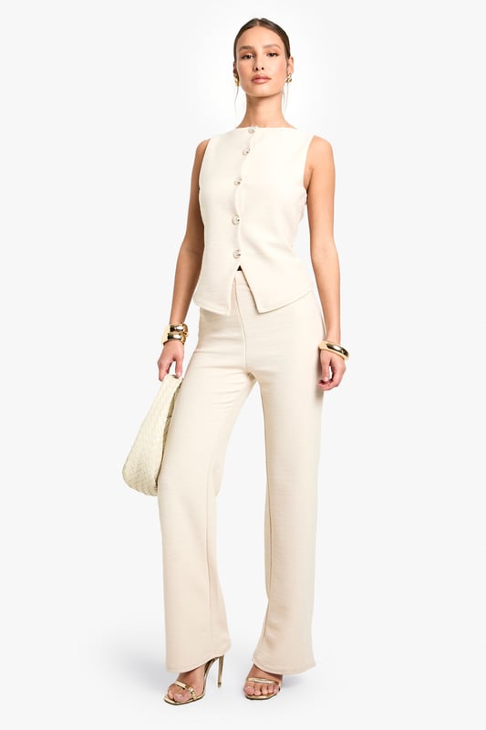 Textured knitted waistcoat with elegant boat neckline for a sophisticated silhouette
        Sleeveless design with clean-cut edges perfect for layering or wearing alone
        Decorative button-through front with distinctive statement buttons
        Structured fit that gently contours the body for a flattering shape
        Versatile length that pairs beautifully with coordinating trousers or contrasting bottoms
    
    This textured waistcoat reimagines casual dressing with its contemporary structured design. The sleek boat neckline and decorative button detailing create a refined aesthetic that transitions effortlessly from day to evening. Style with the matching trousers as seen on our model for a coordinated ensemble that works brilliantly for family gatherings or casual brunches. For a more relaxed approach, pair with wide-leg jeans and trainers, adding layered gold jewellery for a touch of everyday glamour. The versatile nature of this piece allows for customisation to suit your personal style - try layering over a fitted long-sleeve top when temperatures drop or wearing alone with statement accessories for warmer days. Perfect for those seeking a polished yet comfortable look for casual occasions.