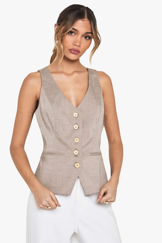 Tailored waistcoat featuring distinctive wooden buttons for a natural touch
        Sleek V-neckline creates an elegant silhouette perfect for layering
        Contoured fit with subtle waist definition for a flattering shape
        Versatile sleeveless design ideal for year-round styling
        Woven fabric with slight stretch ensures comfort throughout the day
    
    This sophisticated waistcoat brings tailored refinement to any ensemble. The wooden button detailing adds a distinctive character to this otherwise classic piece, making it perfect for occasions that demand polished style. Pair with crisp white wide-leg trousers as shown for a contemporary take on formal dressing, or layer over a fitted blouse for added dimension. For summer events, style with a printed neck scarf and statement accessories for a fashion-forward look. The versatile design transitions seamlessly from office to evening, making it an essential wardrobe investment. For formal occasions such as graduations or race days, complement with tailored trousers and delicate jewellery for an ensemble that conveys understated elegance. The structured silhouette creates a refined look whilst maintaining comfort for all-day wear.