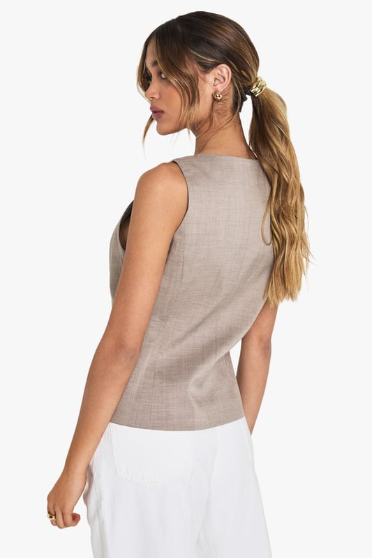 Tailored waistcoat featuring distinctive wooden buttons for a natural touch
        Sleek V-neckline creates an elegant silhouette perfect for layering
        Contoured fit with subtle waist definition for a flattering shape
        Versatile sleeveless design ideal for year-round styling
        Woven fabric with slight stretch ensures comfort throughout the day
    
    This sophisticated waistcoat brings tailored refinement to any ensemble. The wooden button detailing adds a distinctive character to this otherwise classic piece, making it perfect for occasions that demand polished style. Pair with crisp white wide-leg trousers as shown for a contemporary take on formal dressing, or layer over a fitted blouse for added dimension. For summer events, style with a printed neck scarf and statement accessories for a fashion-forward look. The versatile design transitions seamlessly from office to evening, making it an essential wardrobe investment. For formal occasions such as graduations or race days, complement with tailored trousers and delicate jewellery for an ensemble that conveys understated elegance. The structured silhouette creates a refined look whilst maintaining comfort for all-day wear.