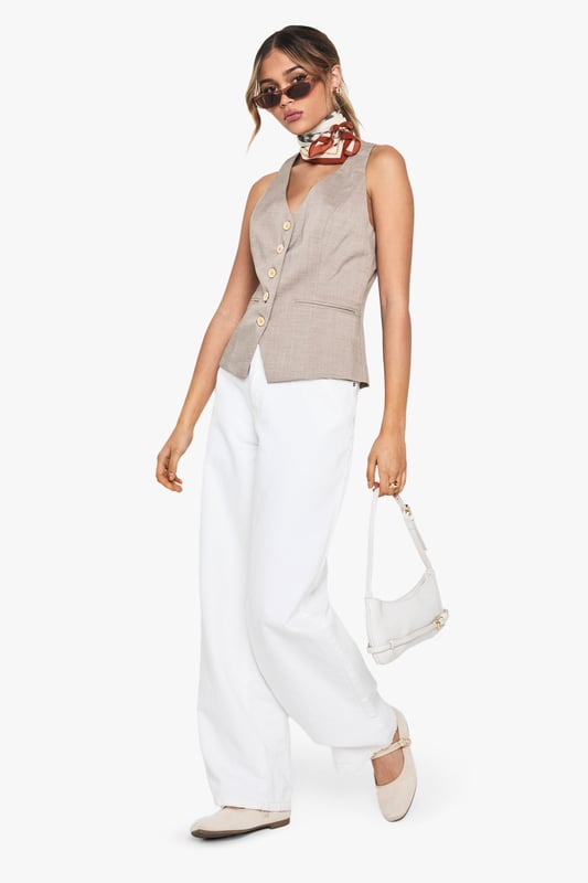 Tailored waistcoat featuring distinctive wooden buttons for a natural touch
        Sleek V-neckline creates an elegant silhouette perfect for layering
        Contoured fit with subtle waist definition for a flattering shape
        Versatile sleeveless design ideal for year-round styling
        Woven fabric with slight stretch ensures comfort throughout the day
    
    This sophisticated waistcoat brings tailored refinement to any ensemble. The wooden button detailing adds a distinctive character to this otherwise classic piece, making it perfect for occasions that demand polished style. Pair with crisp white wide-leg trousers as shown for a contemporary take on formal dressing, or layer over a fitted blouse for added dimension. For summer events, style with a printed neck scarf and statement accessories for a fashion-forward look. The versatile design transitions seamlessly from office to evening, making it an essential wardrobe investment. For formal occasions such as graduations or race days, complement with tailored trousers and delicate jewellery for an ensemble that conveys understated elegance. The structured silhouette creates a refined look whilst maintaining comfort for all-day wear.