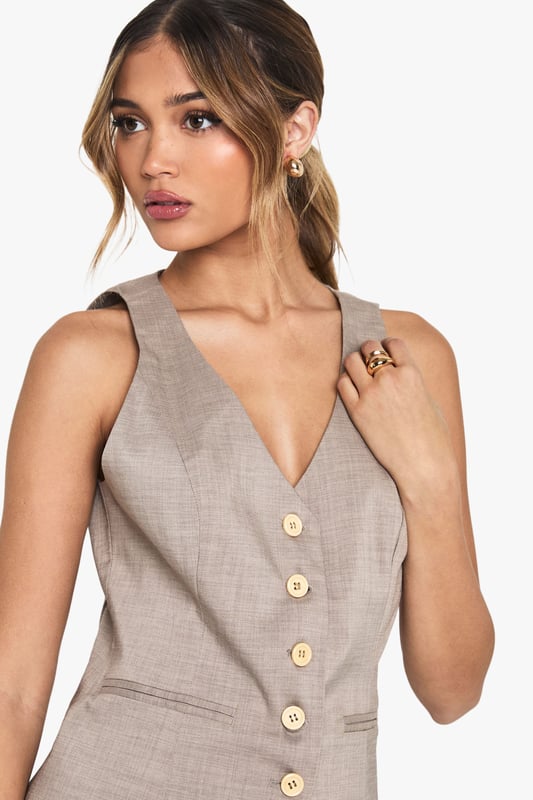 Tailored waistcoat featuring distinctive wooden buttons for a natural touch
        Sleek V-neckline creates an elegant silhouette perfect for layering
        Contoured fit with subtle waist definition for a flattering shape
        Versatile sleeveless design ideal for year-round styling
        Woven fabric with slight stretch ensures comfort throughout the day
    
    This sophisticated waistcoat brings tailored refinement to any ensemble. The wooden button detailing adds a distinctive character to this otherwise classic piece, making it perfect for occasions that demand polished style. Pair with crisp white wide-leg trousers as shown for a contemporary take on formal dressing, or layer over a fitted blouse for added dimension. For summer events, style with a printed neck scarf and statement accessories for a fashion-forward look. The versatile design transitions seamlessly from office to evening, making it an essential wardrobe investment. For formal occasions such as graduations or race days, complement with tailored trousers and delicate jewellery for an ensemble that conveys understated elegance. The structured silhouette creates a refined look whilst maintaining comfort for all-day wear.