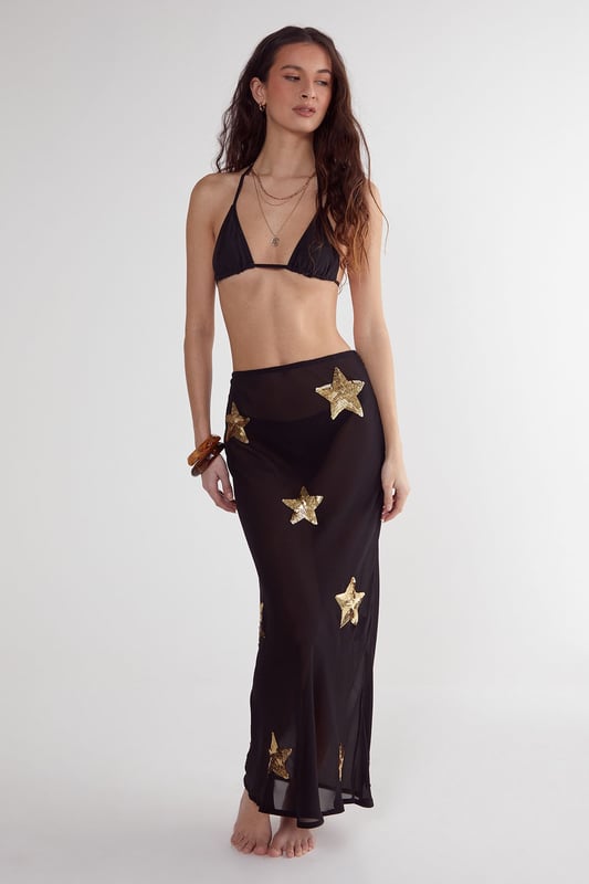 Midi-length beach skirt featuring eye-catching star sequin embellishments
        Lightweight woven fabric perfect for warm-weather destinations
        Flattering silhouette with a comfortable fit that moves with you
        Sheer design ideal for layering over swimwear
        Versatile piece that transitions effortlessly from beach to bar
    
    Make a statement on your next beach holiday with this show-stopping Star Embellished Midi Beach Skirt from Nasty Gal. The striking star sequin detailing catches the light beautifully as you stroll along the shoreline or lounge by the pool. Style it as seen with a matching triangle bikini top for a coordinated beach look, or pair with a simple bandeau and oversized sunglasses for effortless glamour. The semi-sheer fabric offers just the right amount of coverage whilst maintaining that essential holiday vibe. Perfect for sunset cocktails, simply add a loose linen shirt and some metallic sandals to transform your daytime beach ensemble into an evening-ready outfit. This skirt is a must-have addition to your holiday wardrobe, promising to turn heads wherever your sunny adventures take you.