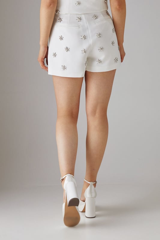 Sophisticated tailored shorts featuring delicate embellishment throughout for a distinctive look
        High-waisted design with a clean, streamlined silhouette for a flattering fit
        Subtle back pockets maintain the sleek aesthetic while offering practicality
        Versatile mid-thigh length perfect for both day and evening occasions
        Slight stretch in the fabric ensures comfort without compromising on structure
    
    These embellished tailored shorts from Warehouse showcase refined craftsmanship with their structured silhouette and eye-catching embellishments. The high-waisted design creates a leg-lengthening effect whilst the tailored cut offers a sophisticated edge to your going-out wardrobe. Style with a matching embellished top as shown for a coordinated set that commands attention, or break up the look with a crisp white blouse for cocktail events. For evening soires, pair with strappy heels and statement jewellery to amplify the glamour. When the temperature drops, layer with a cropped blazer to maintain the polished aesthetic. These shorts transition seamlessly from sunset drinks to late-night dancing, making them a versatile addition to your night-out collection.