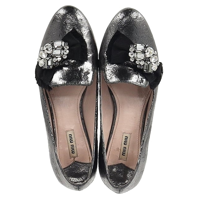 VINTAGE, UVP WIE NEU  
Die Miu Miu von Prada Jeweled Ballerinas aus metallic grauem Leder bieten eine perfekte Fusion aus Komfort und hochwertiger Mode, mit ausgefeilten, mit Edelsteinen besetzten Details für einen Hauch von Luxus. Hergestellt aus weichem metallic grauem Leder, sind diese Ballerinas vielseitig genug, um jedes Outfit zu erhöhen und gleichzeitig ganztägliche Tragbarkeit zu bieten. Kombinieren Sie sie mit einem fließenden Midikleid für einen schicken, femininen Look, oder stylen Sie sie mit maßgeschneiderten Hosen und einer Bluse für eine elegante, raffinierte Ausstrahlung. Der metallische Glanz verleiht einen zeitgemäßen Akzent und macht sie zu einem Statement-Stück, das sowohl zu legerer als auch zu abendlicher Kleidung passt.

Miu Miu von Prada Jeweled Ballerinas aus metallic grauem Leder

Zustand: Sehr gut  
Abnutzungserscheinungen: Einschließlich Box. Leichte Markierungen, Leicht gebraucht, aber sehr gut gepflegt. Kleine Abnutzungsspuren an den Sohlen & Falten, leichte Kratzer an den Sohlen und Fersen.  
Verpackung: Box  
Farbe: Grau  
Material: Leder | Leder  
Größe: IT | 41  
Maßnahmen: Innensohlenlänge: 300  
SKU: NAPPUGBSH465050W