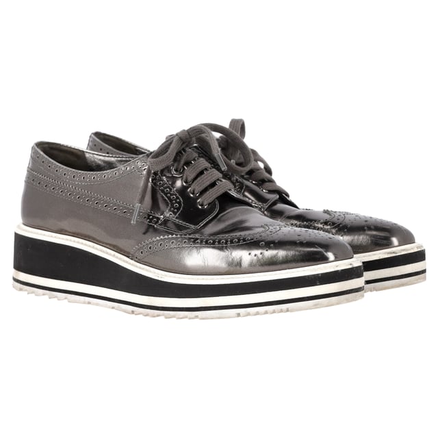 Vintage, Neupreis wie neu  
Bereiten Sie sich darauf vor, Blicke auf sich zu ziehen mit den Prada Metallic Brogue Platform Low Top Sneakers aus silbernem Leder. Diese Sneakers vereinen nahtlos High Fashion und Alltagskomfort. Hergestellt aus luxuriösem metallic Leder, verfügen sie über klassische Wingtip-Brogue-Details und elegante Schnürverschlüsse, die für einen raffinierten, aber lässigen Look sorgen. Die Plattformsohle bietet zusätzliche Höhe und eine einzigartige Note, während die bequemen Einlegesohlen für einen gepolsterten Tragekomfort den ganzen Tag über sorgen. Kombinieren Sie diese Sneakers mit einem plissierten Midirock und einem Blazer für eine unerwartete Mischung aus formell und lässig oder setzen Sie auf einen monochromen Look mit einer silberfarbenen Jacke und maßgeschneiderten Hosen, um das metallische Thema durchgehend zu gestalten.

mit Staubbeutel

Prada Metallic Brogue Platform Low Top Sneakers aus silbernem Leder  
Zustand: Sehr gut  
Tragespuren: Leicht gebraucht, aber sehr gut gepflegt. Kleine Makel an den Sohlen & Faltenbildung, leichte Abnutzung an den Sohlen und Absätzen. Keine sichtbaren Abnutzungsspuren. Kein Makel an der Einlegesohle.  
Verpackung: Staubbeutel  
Farbe: Silber  
Material: Leder | Leder  
Größe: EU | 40,5  
Maße: Absatzhöhe: 50; Einlegesohlenlänge: 290  
SKU: NAPPUGBSH462916W