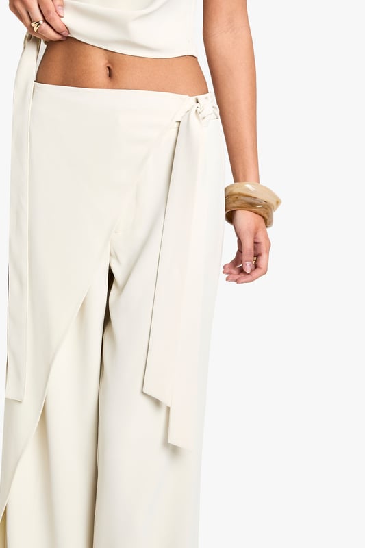 Wrap-style trousers with straight leg design
        Distinctive tie detail at the waist
        High-waisted silhouette for a flattering fit
        Flowing crepe fabric for effortless movement
        Versatile piece suitable for various occasions
    
    Make a statement with these chic wrap-style trousers, perfect for the fashion-forward woman who loves to stand out. The straight leg cut offers a modern twist on a classic silhouette, while the eye-catching tie detail at the waist adds a touch of drama. Pair these trousers with a cropped top and strappy heels for a night out with friends, or dress them down with a simple tee and trainers for a more casual look. The high-waisted design elongates your legs and cinches in your waist, creating a sleek and sophisticated silhouette. Whether you're heading to a trendy rooftop bar or meeting up for cocktails, these trousers will ensure you're always dressed to impress. The flowing crepe fabric moves beautifully with every step, making them ideal for dancing the night away or simply strutting your stuff on the city streets.