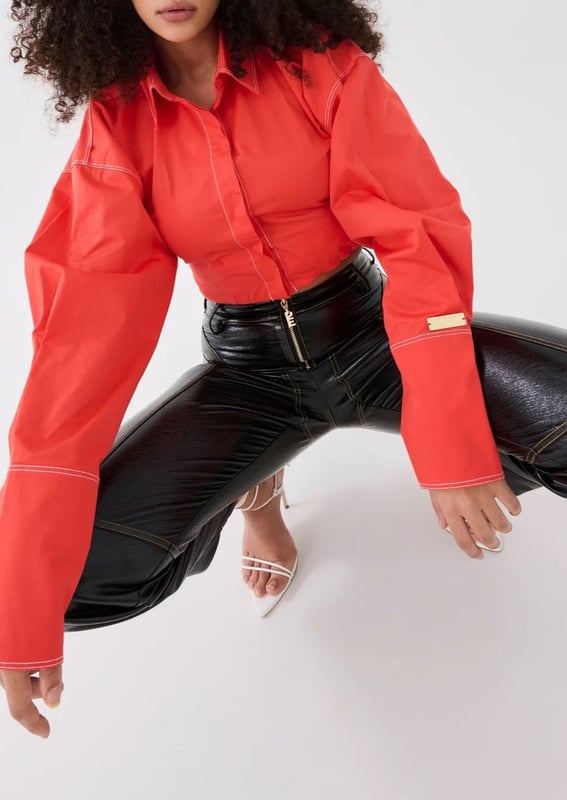 100% Cotton. Cropped fit with a concealed centre front button closure. Contrasting white stitching. Exaggerated sleeves and elongated cuffs. Elasticated around the waist